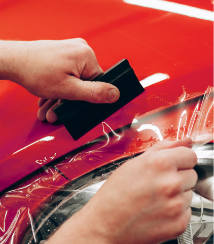 Hands applying Cosmo PPF film to red paint
